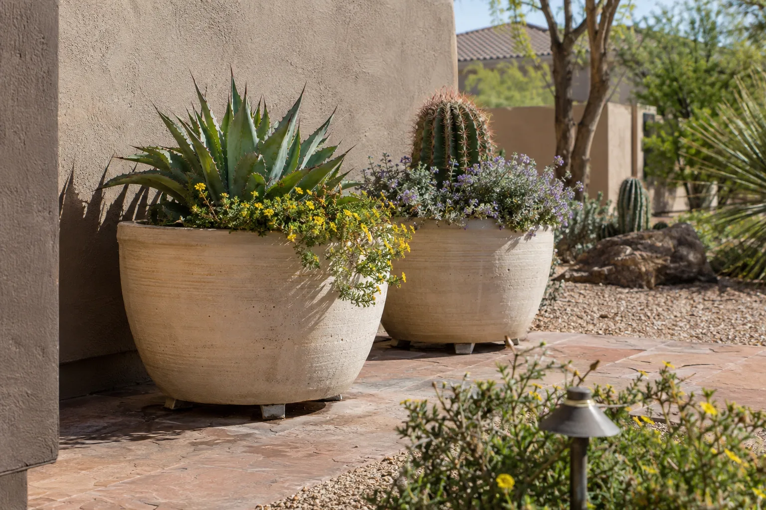 Light-colored ceramic planters raised on pot feet beside a stucco wall in desert sun