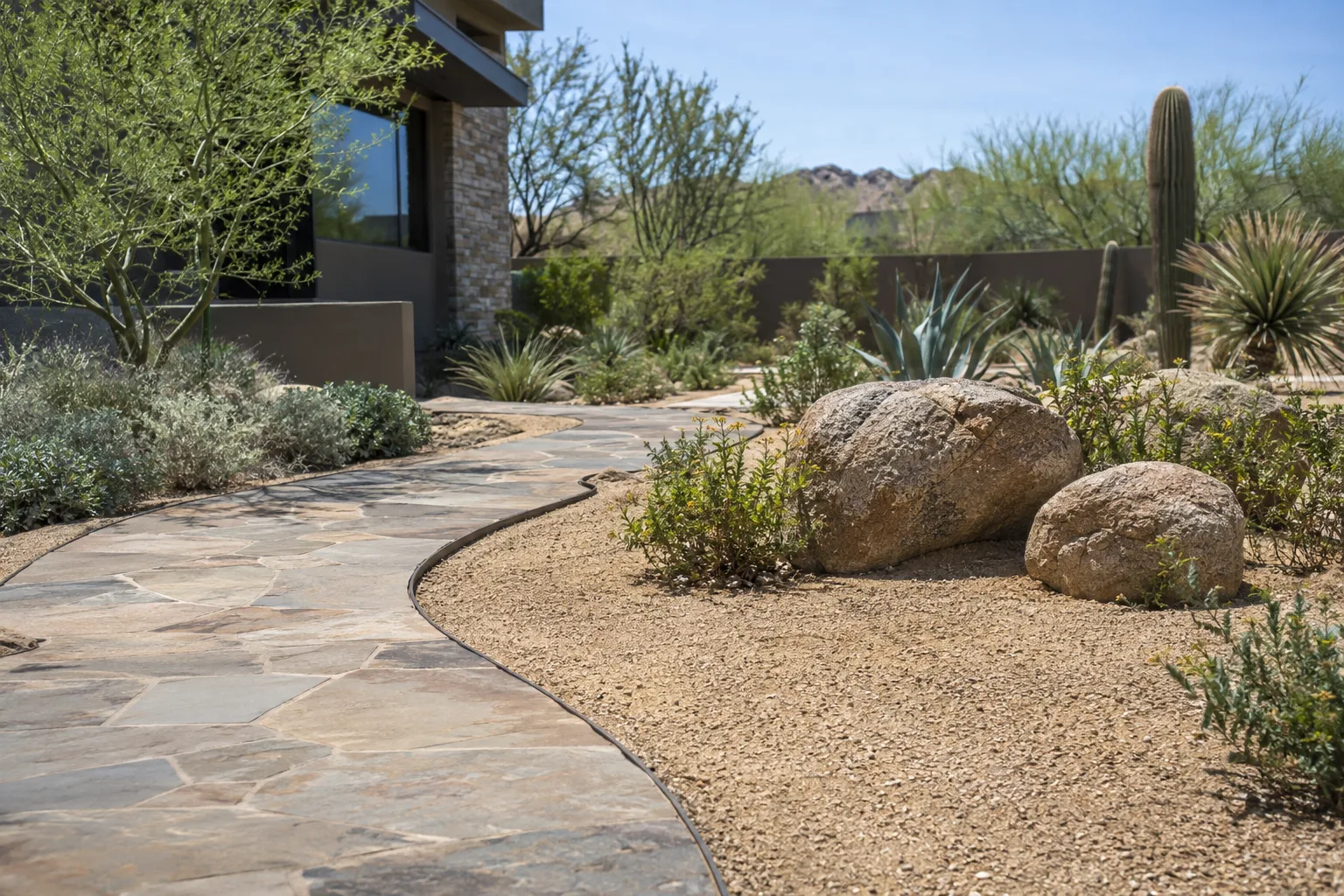 Flagstone path with steel edging, tan gravel and a group of three boulders in a yard